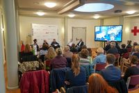 Mehrere Dutzend Menschen schauen sich eine Gesprächsrunde von 5 Menschen an.